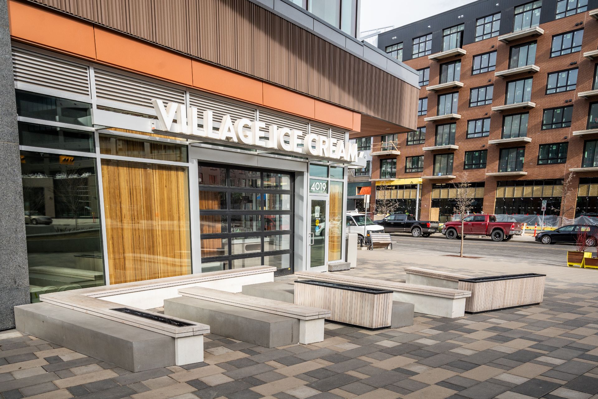 Street-level view of Village Ice Cream in Calgary, Alberta, surrounded by contemporary mixed-use buildings and an urban pedestrian plaza.