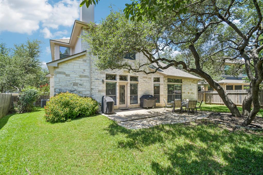 Private backyard and stone patio shaded by mature live oaks at 8008 Ladera Verde Dr