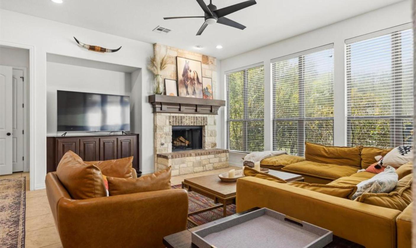 Furnished living room with stone fireplace and wall of windows at 17312 Wildrye Dr, Rocky Creek Ranch lease