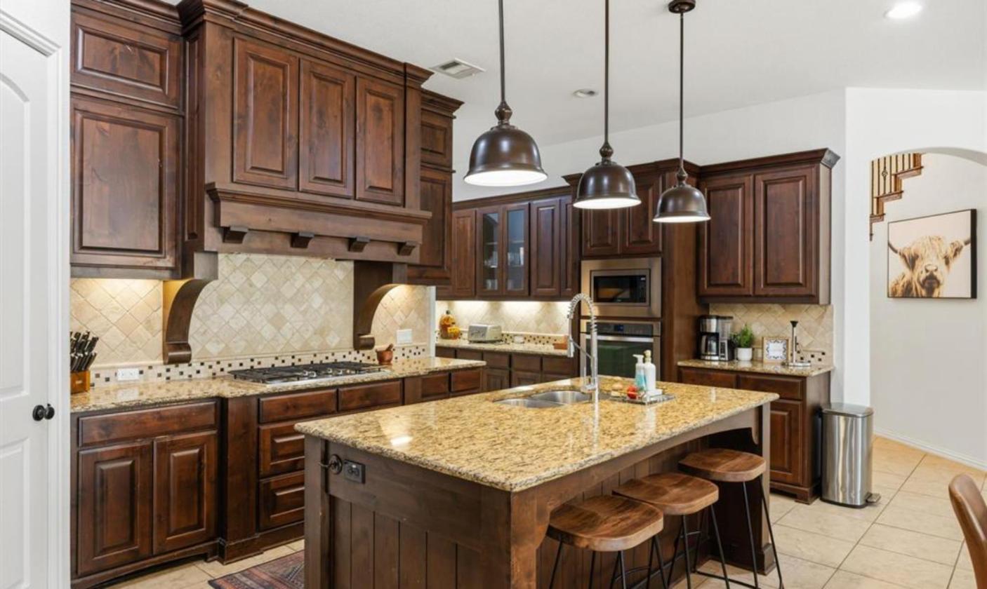 Kitchen with knotty alder cabinets, granite island and gas cooktop at 17312 Wildrye Dr, Austin TX 78738
