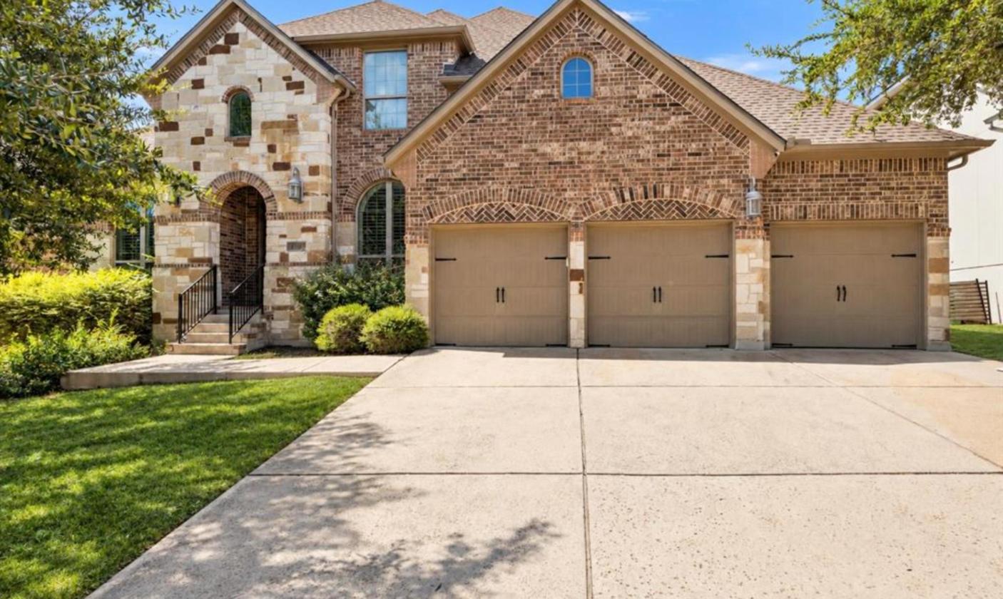 Stone and brick exterior with three-car garage at 17312 Wildrye Dr in Rocky Creek Ranch, Austin TX 78738