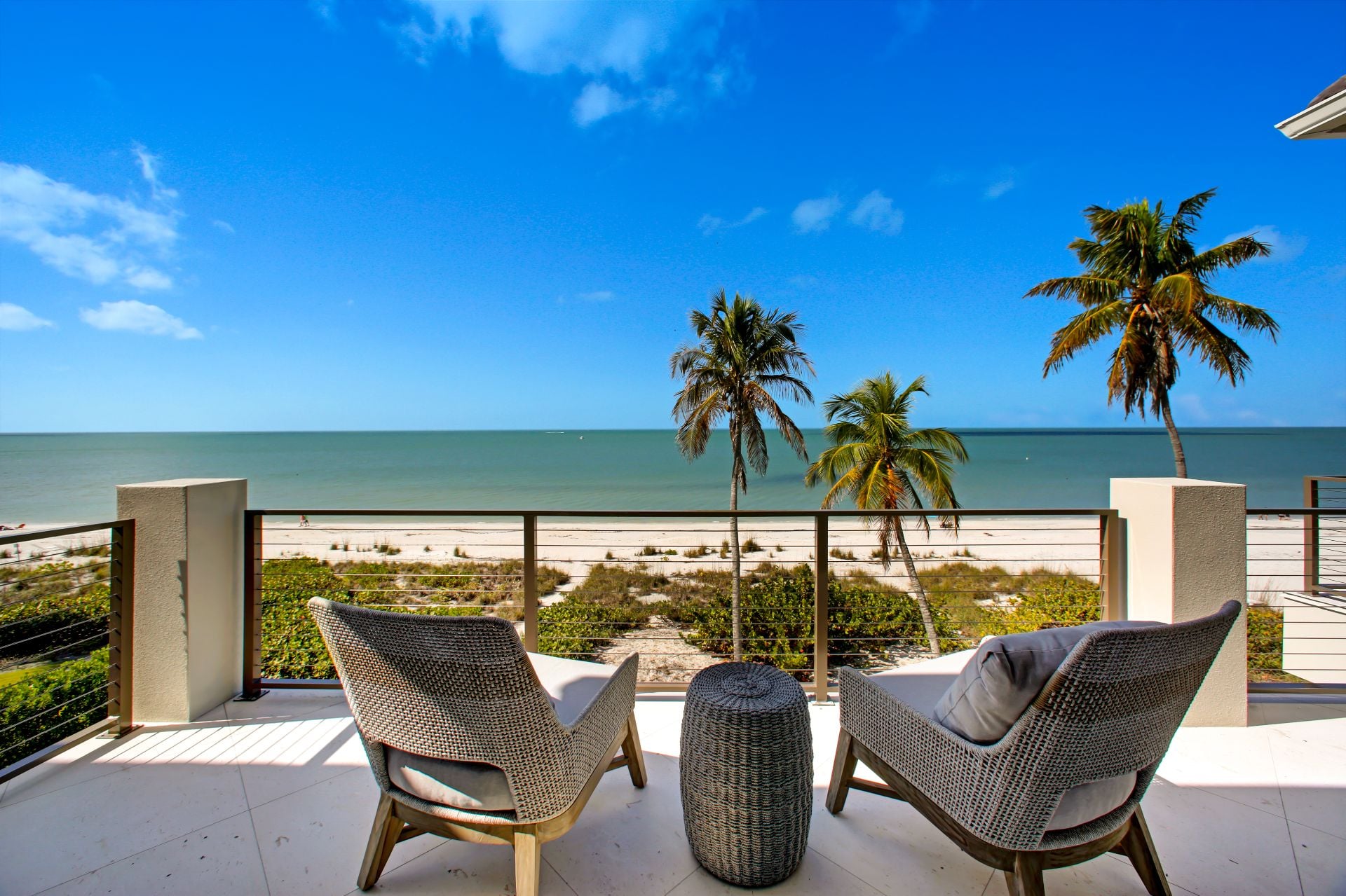 Two chairs on a balcony overlooking the beach in Florida with a grass covered backyard and sand beyond