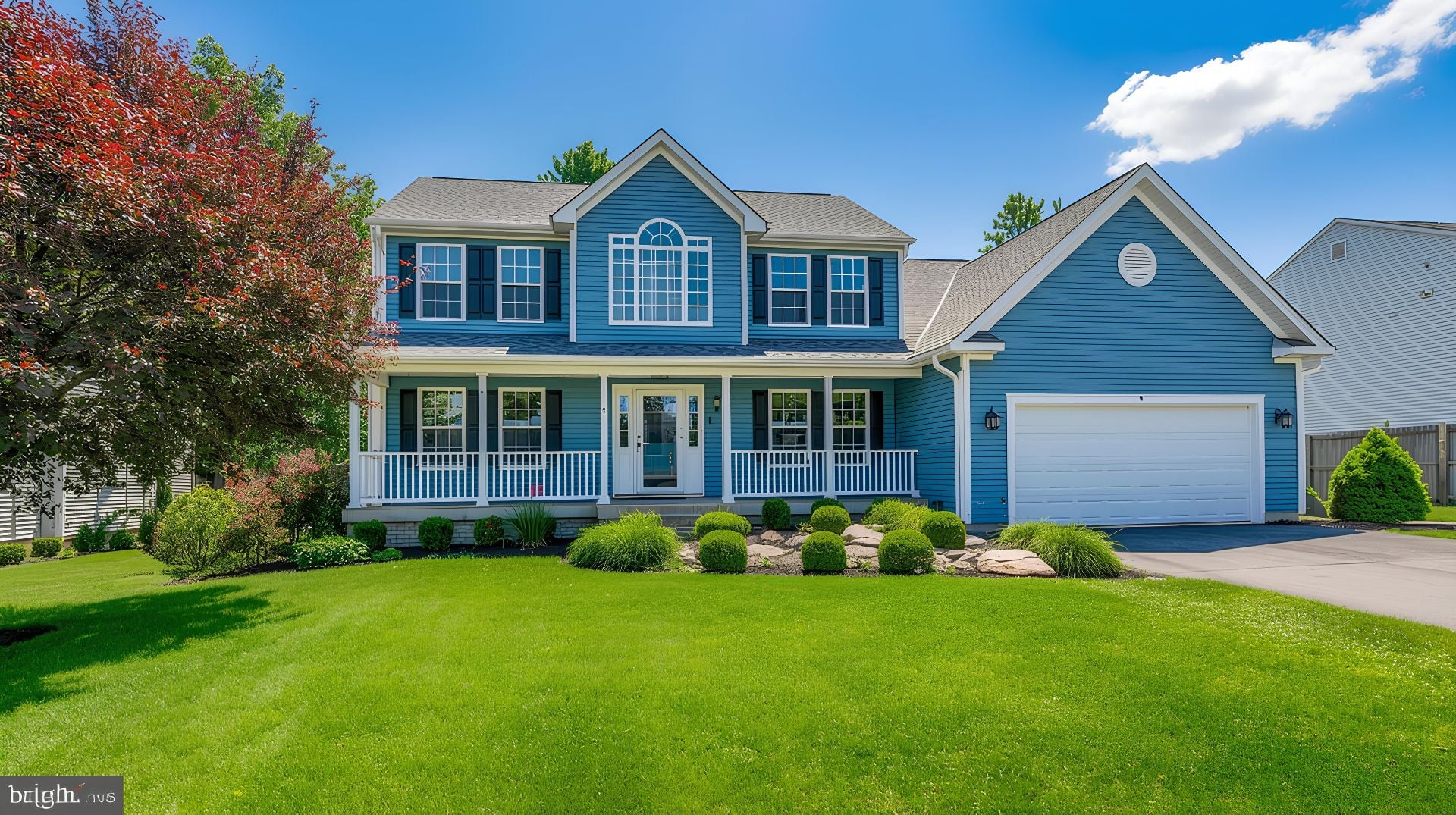 Blue siding residential home exterior featuring white porch columns large front yard green grass manicured landscaping sunny sky suburban architecture