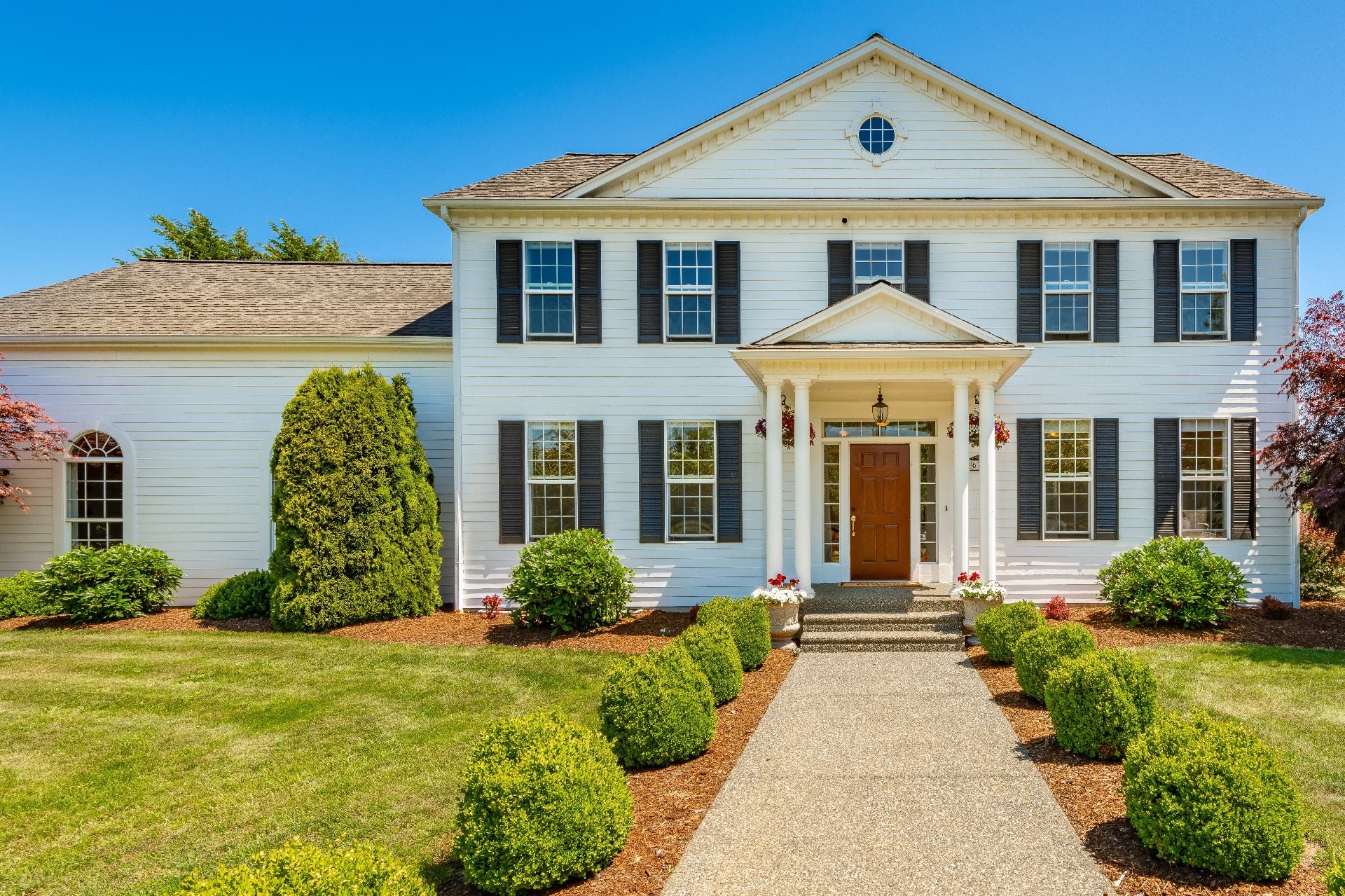 Stately colonial style estate home set agains beautiful blue sky expansive yard