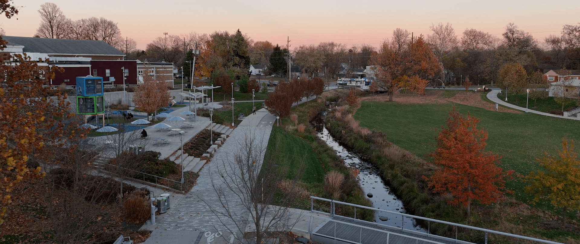 Aerial view of a park in Greenwood, Indiana, with walking paths, green space, creek, and colorful autumn trees.