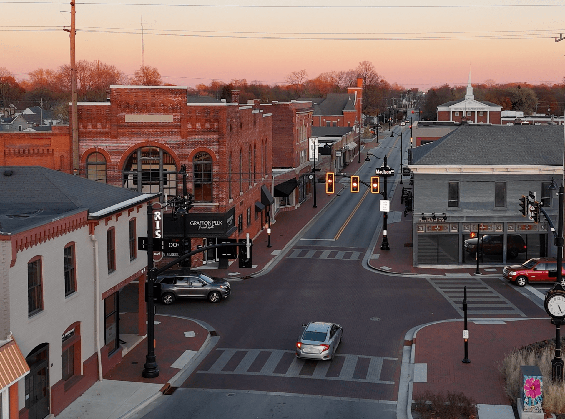 Aerial view of downtown Greenwood, Indiana, with historic brick buildings, intersection, and evening sky in the background.