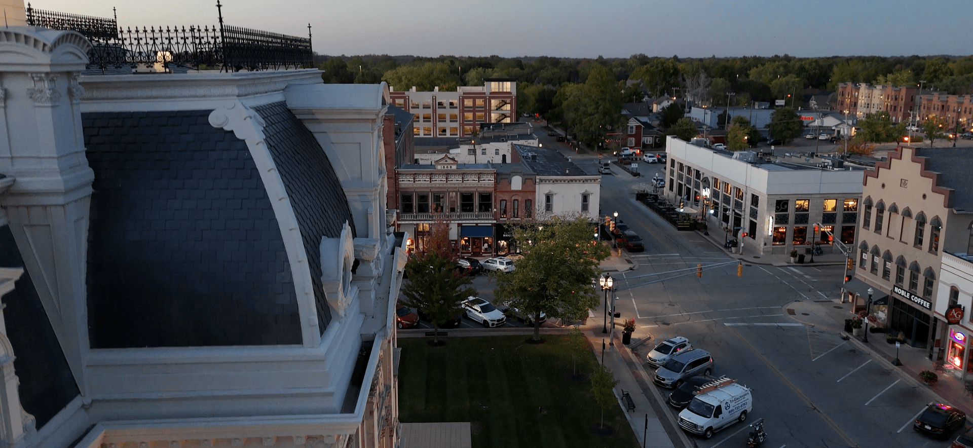 Aerial view of downtown Noblesville, Indiana, featuring historic architecture, local businesses, and a central street intersection at dusk.