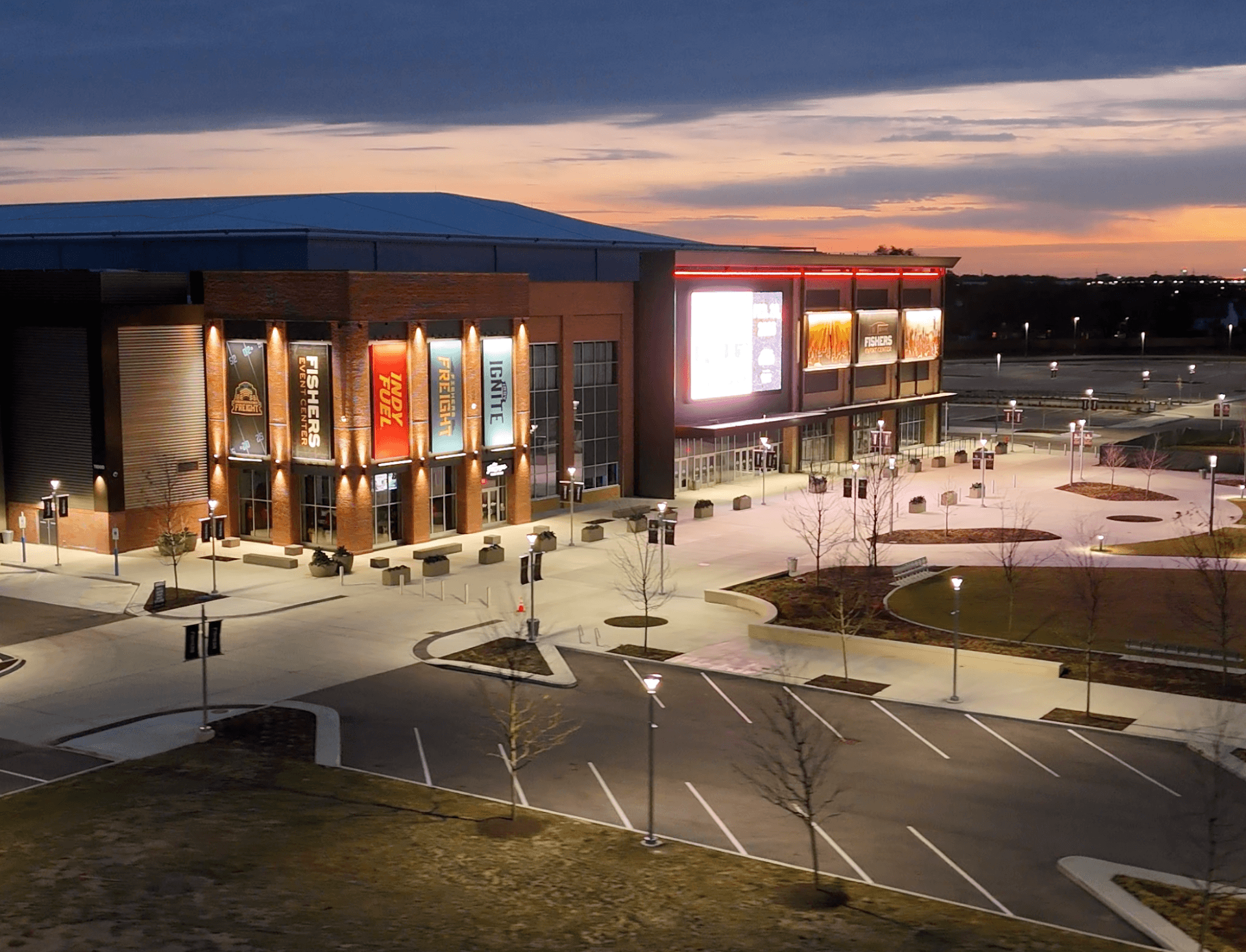 Close aerial view of the Fishers Event Center at sunset with lit facade and surrounding plaza.
