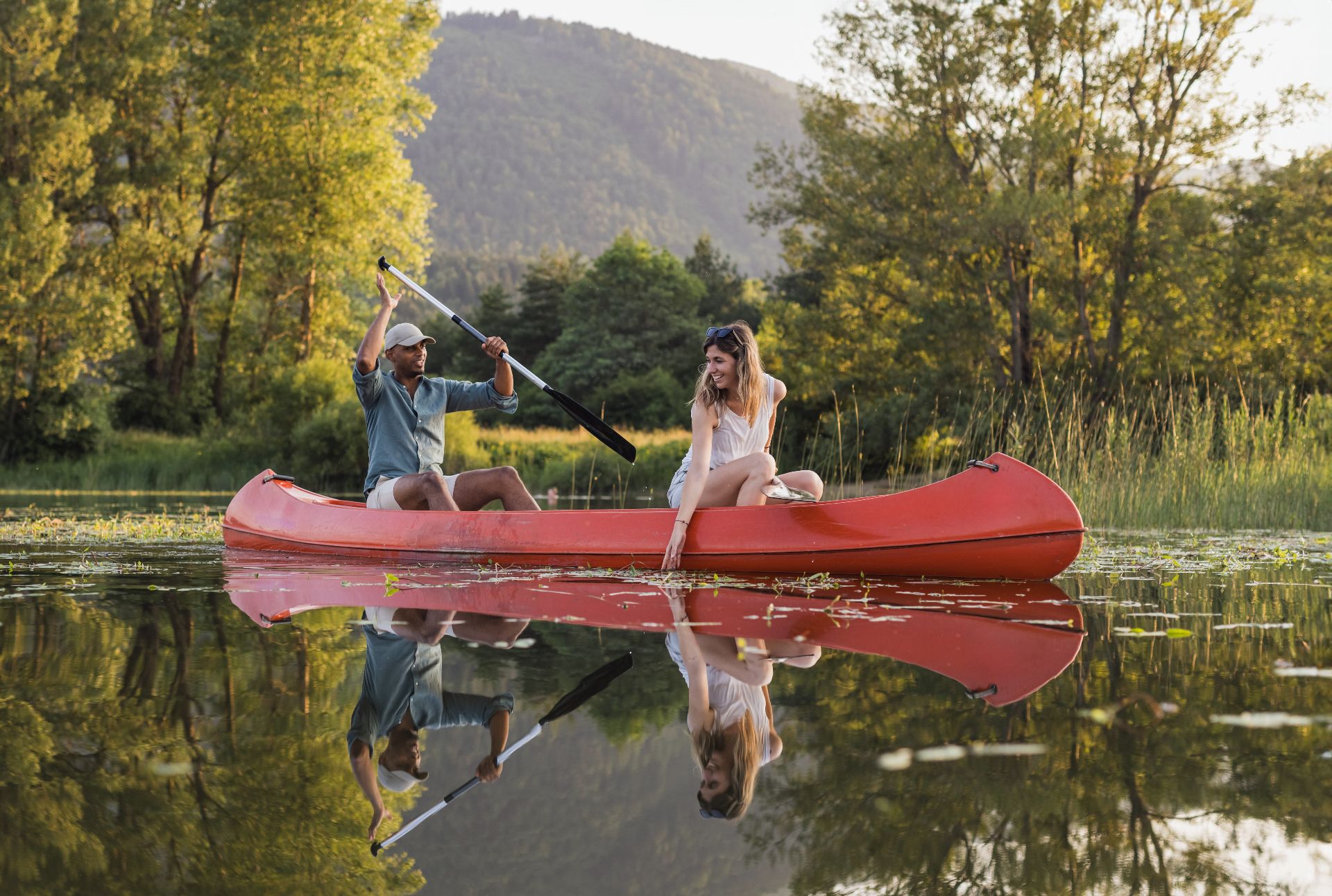 Young couple paddling a canoe on the beautiful calm lake, enjoying a fun adventure of canoeing trip. Summer holiday concept