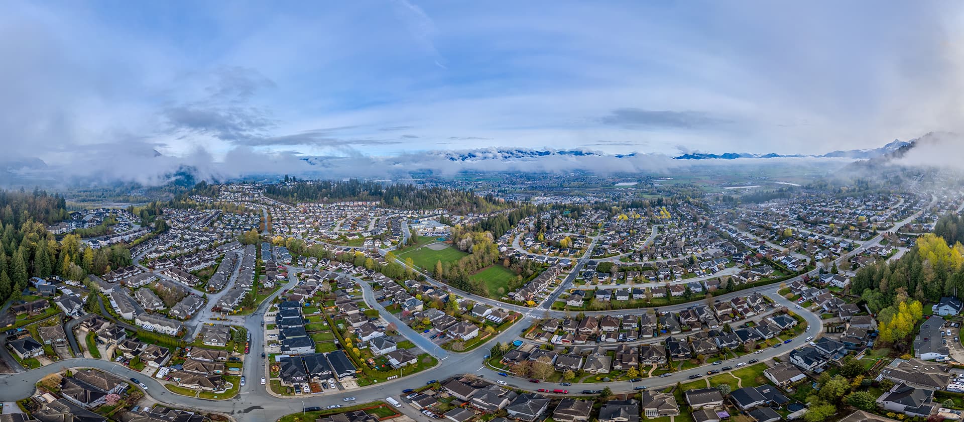 Aerial panoramic view of Chilliwack residential suburbs, parks and surrounding mountains under low clouds in British Columbia, Canada. (1)