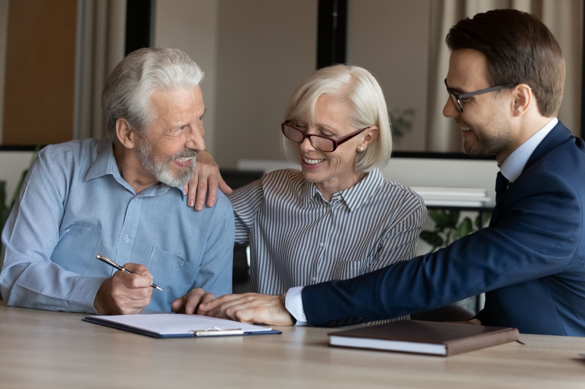 Excited mature couple signing contract with businessman manager realtor broker, making great investment or insurance deal at meeting, happy senior family purchasing real estate, taking loan
