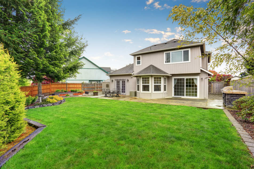 Spacious backyard garden of large beige house with green lawn and Cozy patio area.