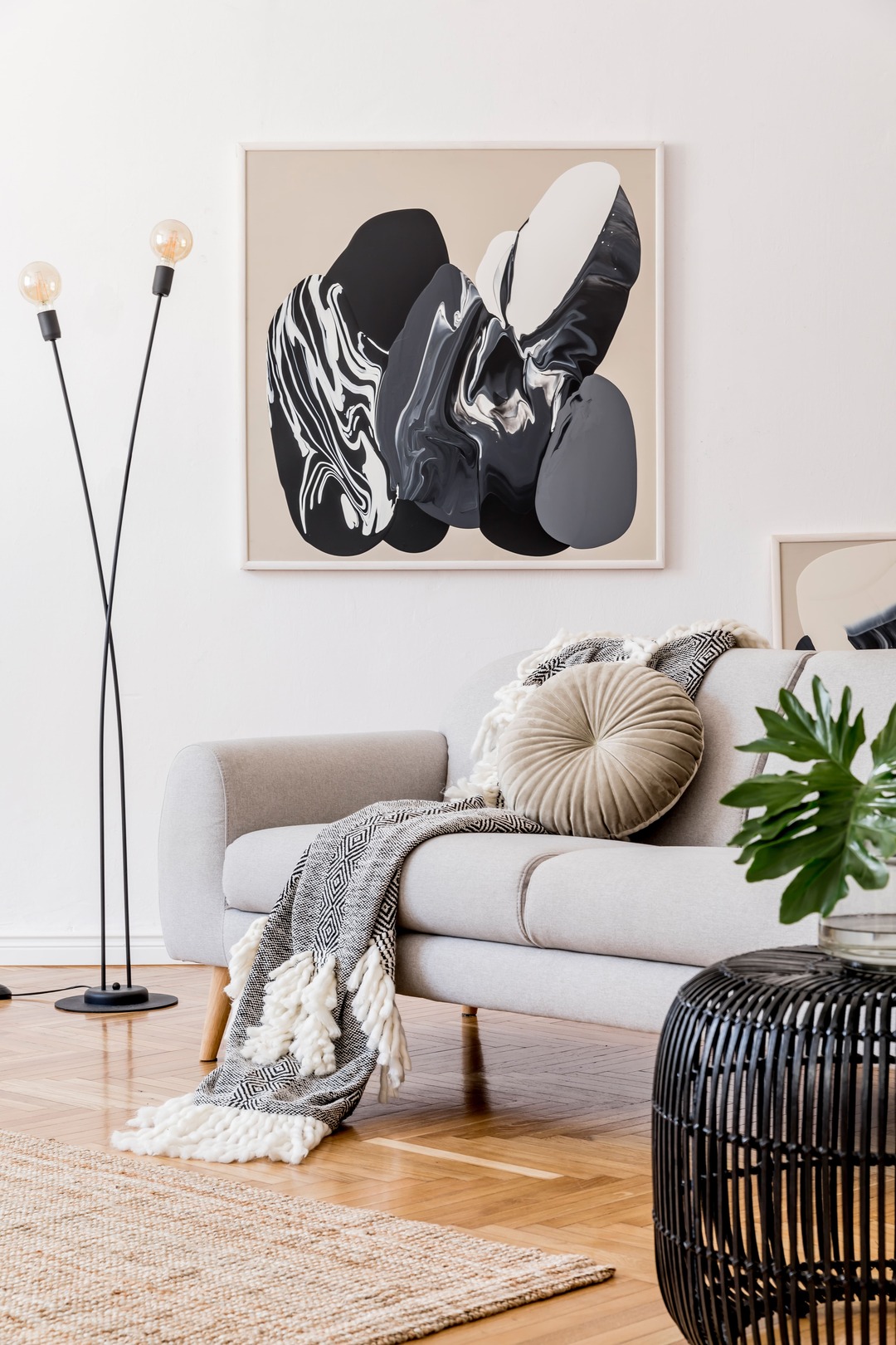 Stylish and design home interior of living room with gray sofa, rattan table, lamp, tropical leaf, plaid, pillows and elegant decoration. Abstract mock up paintings frame on white walls. Template.