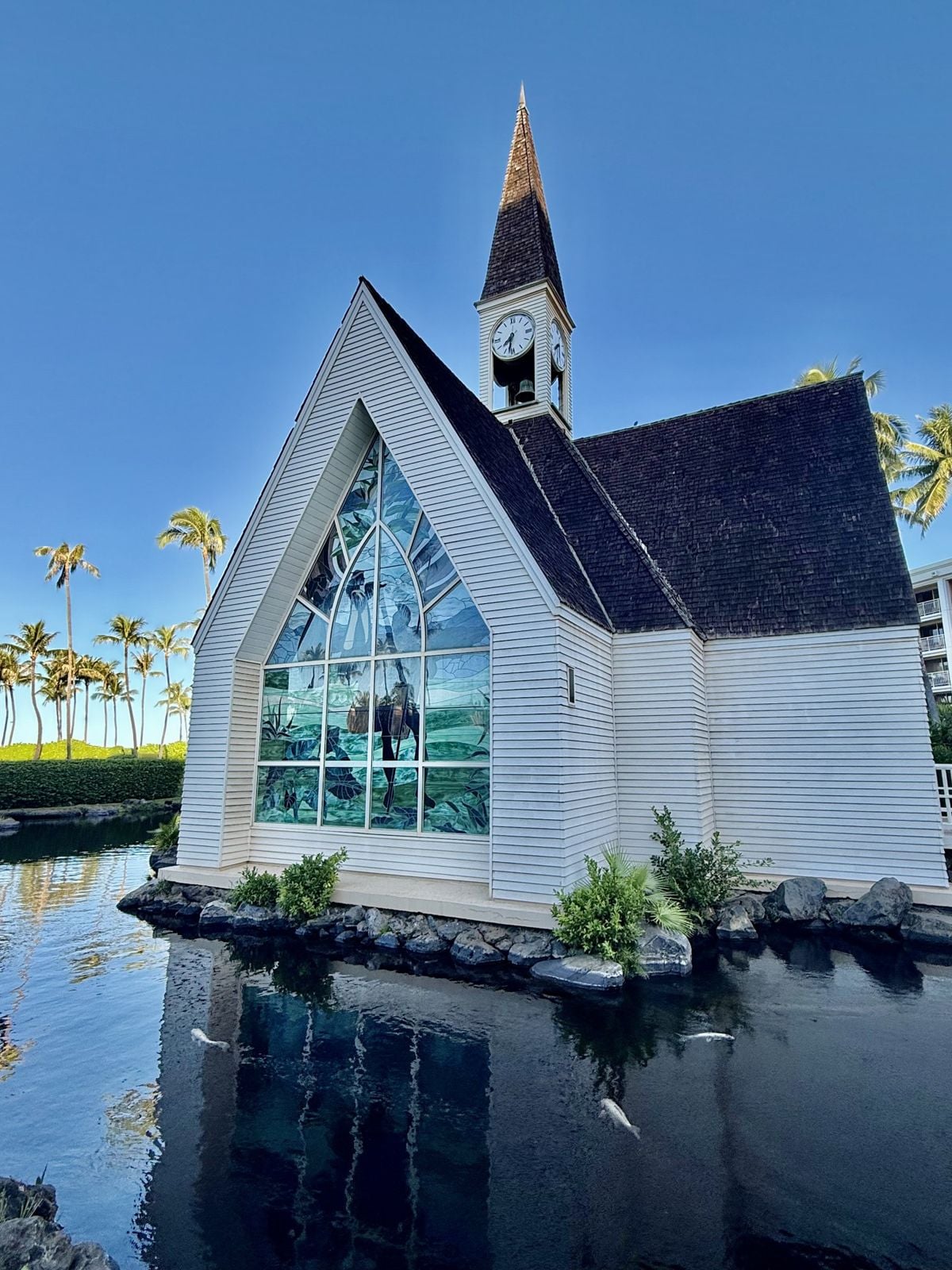 White clapboard chapel with a slender spire and a large stained-glass window, set on a pond at Grand Wailea, Maui
