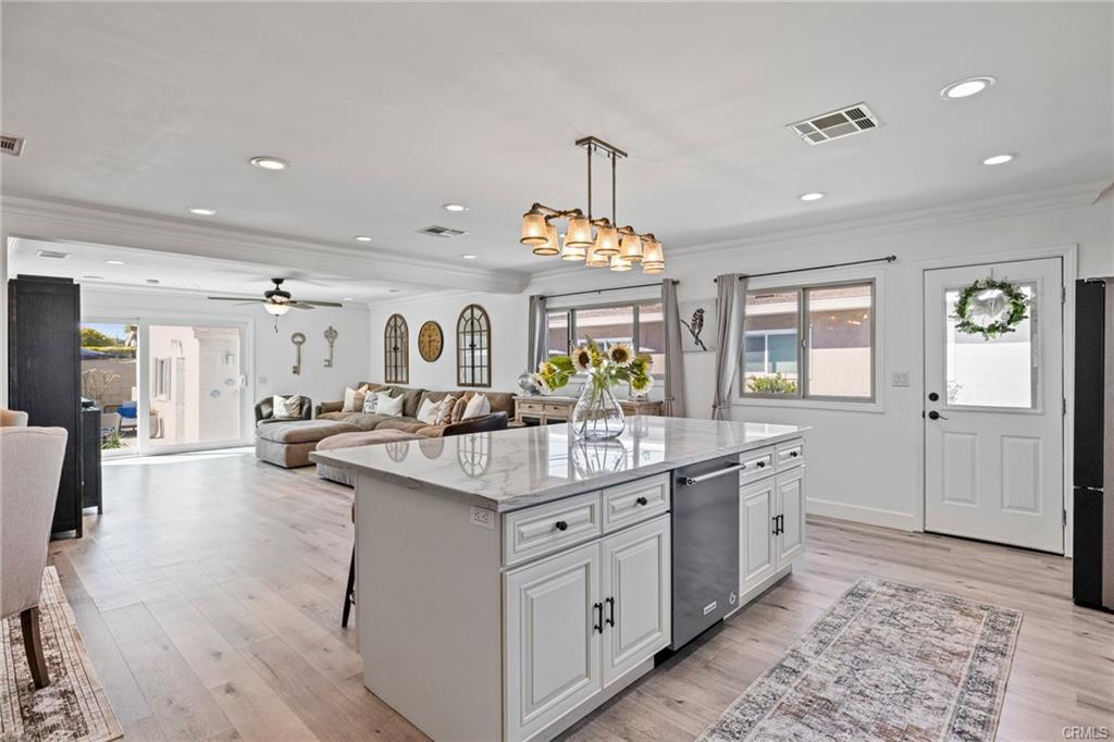 Bright open-concept kitchen and living room with white cabinetry, marble island, recessed lighting, and sliding glass doors leading to an outdoor patio.