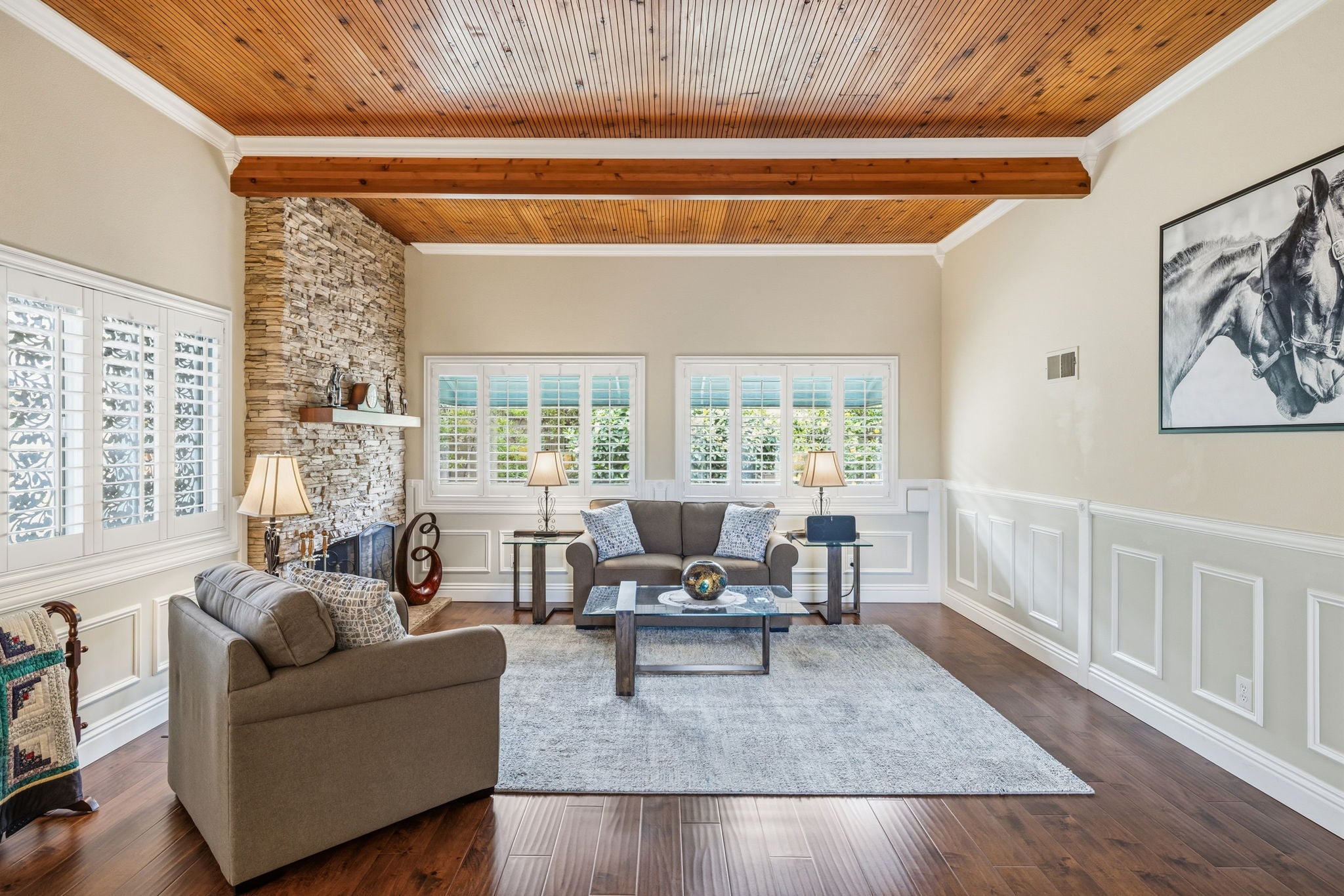Elegant living room with vaulted wood-beam ceiling, stone fireplace, hardwood floors, and large shuttered windows.