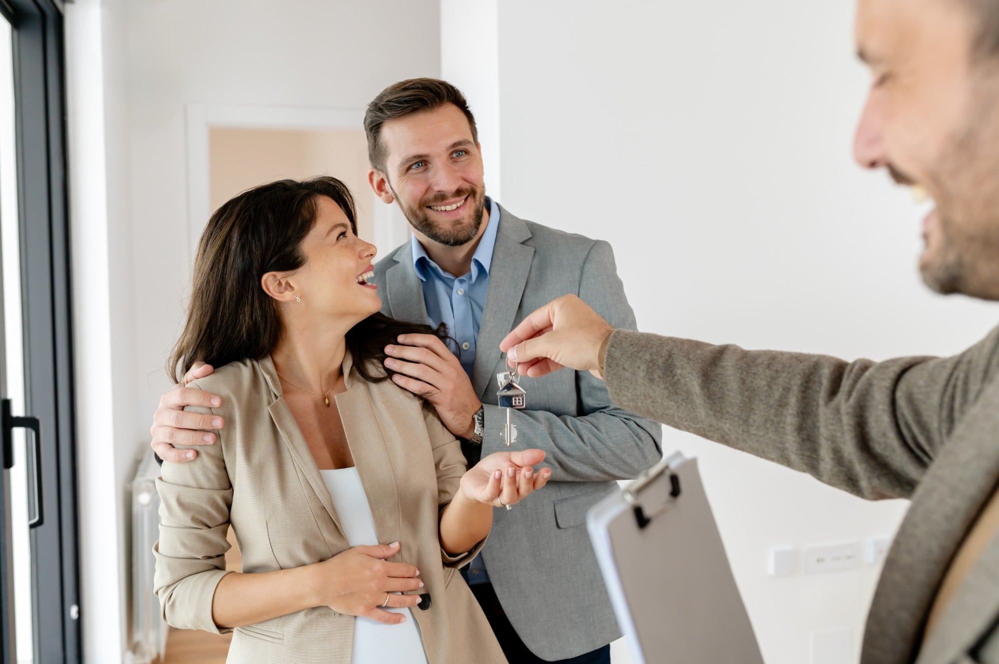 A young, beautiful, and cheerful couple, a man and his pregnant wife, talking with a real-estate agent visiting apartment for sale or for rent