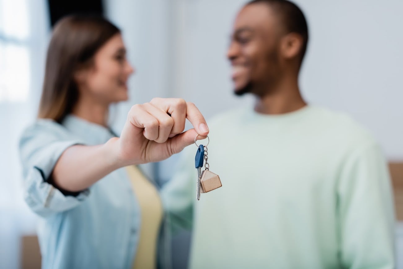 blurred and happy woman holding key near african american man in new apartment
