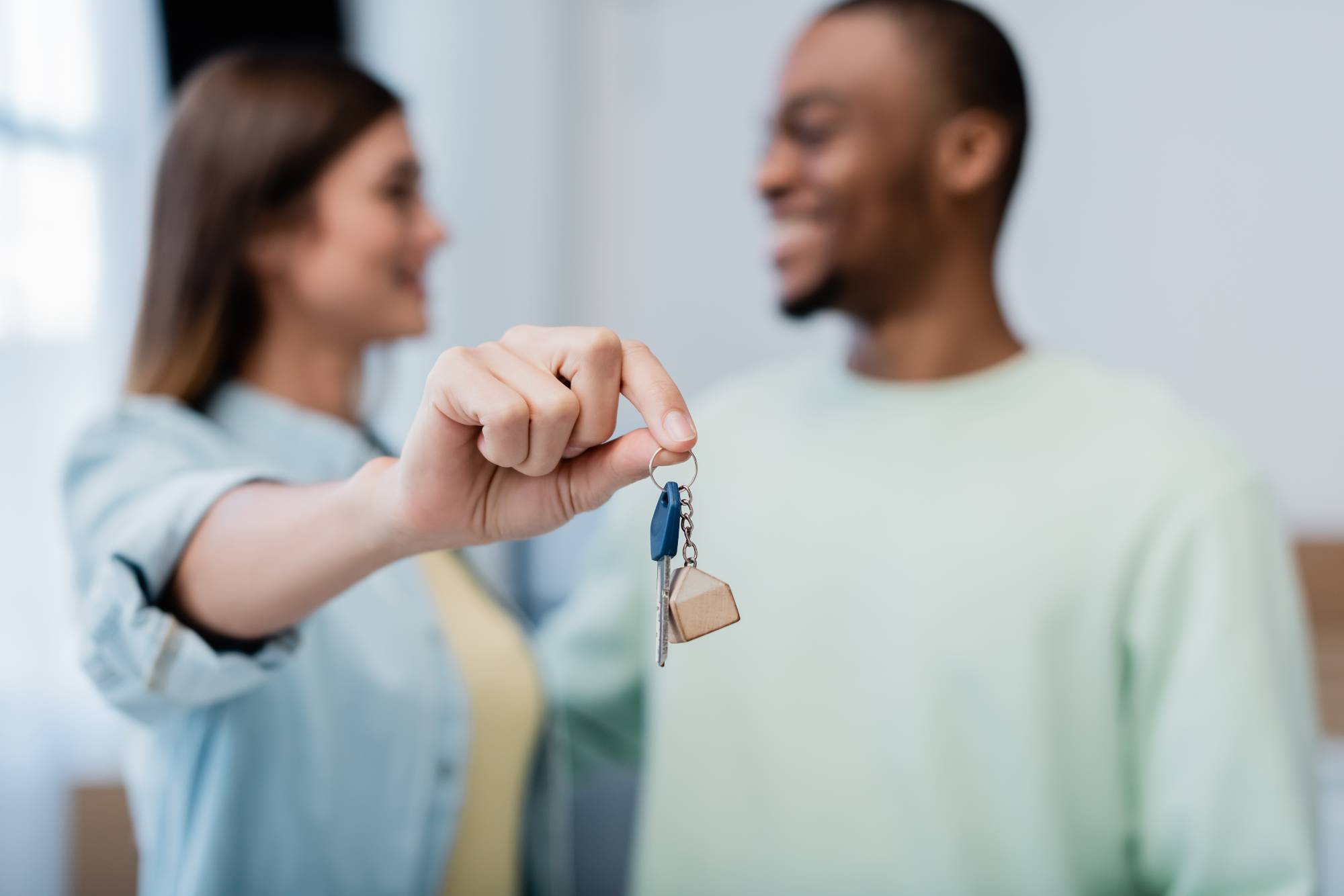 blurred and happy woman holding key near african american man in new apartment