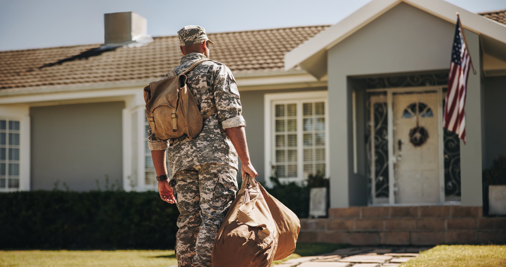 Patriotic-young-soldier-walking-towards-his-house-with-his-luggage.-Rearview-of-an-American-serviceman-coming-back-home-after-serving-in-the-military.