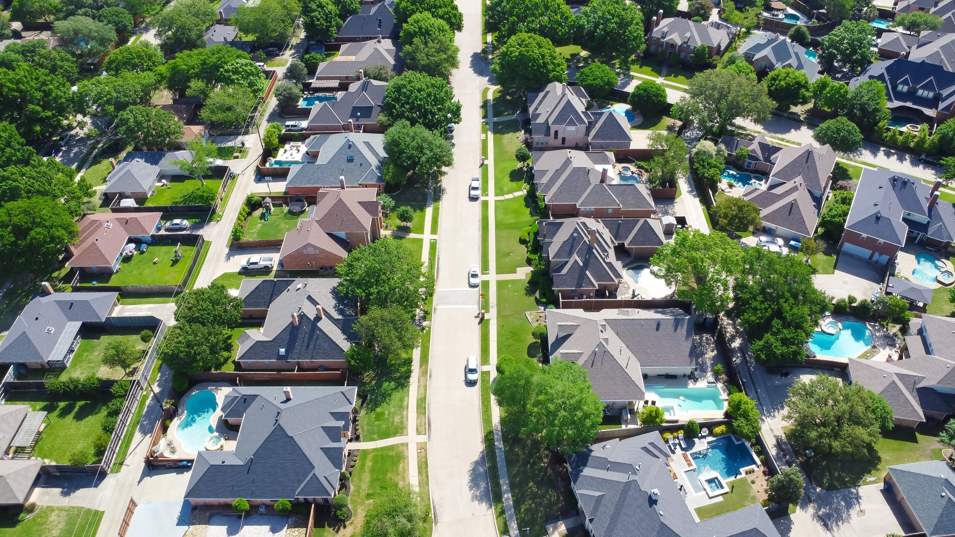 Tree lined residential street with well-trimmed front yard of upscale two-story suburban houses with swimming pool, large fenced backyard, well-trimmed HOA landscape, Dallas, Texas, aerial view. USA