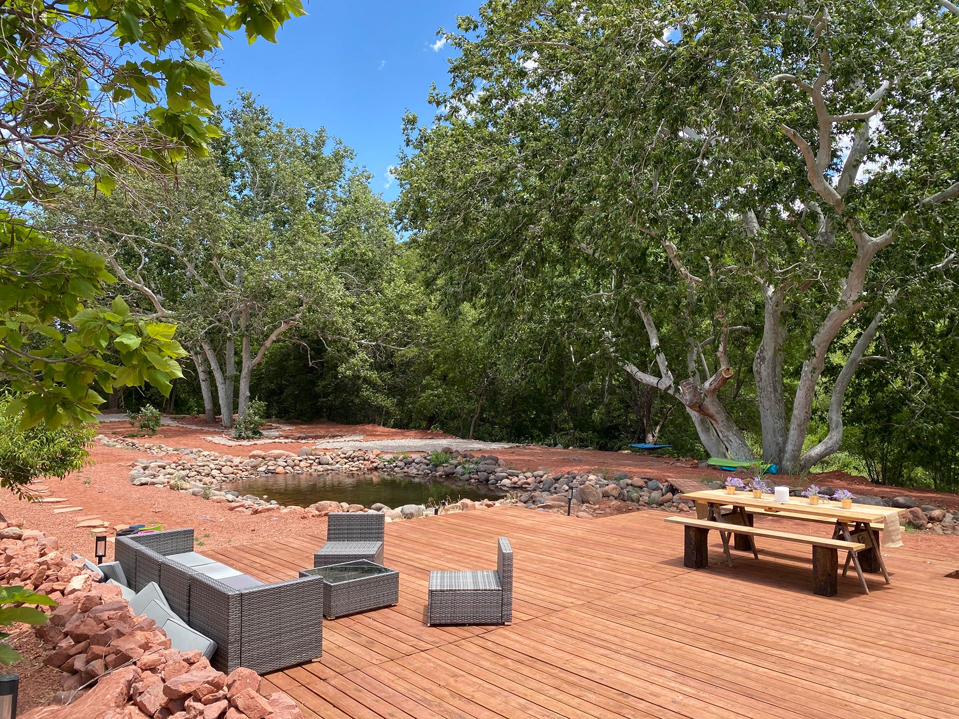 Private Sedona backyard retreat with wood deck, outdoor seating, mature trees, and natural red rock landscaping