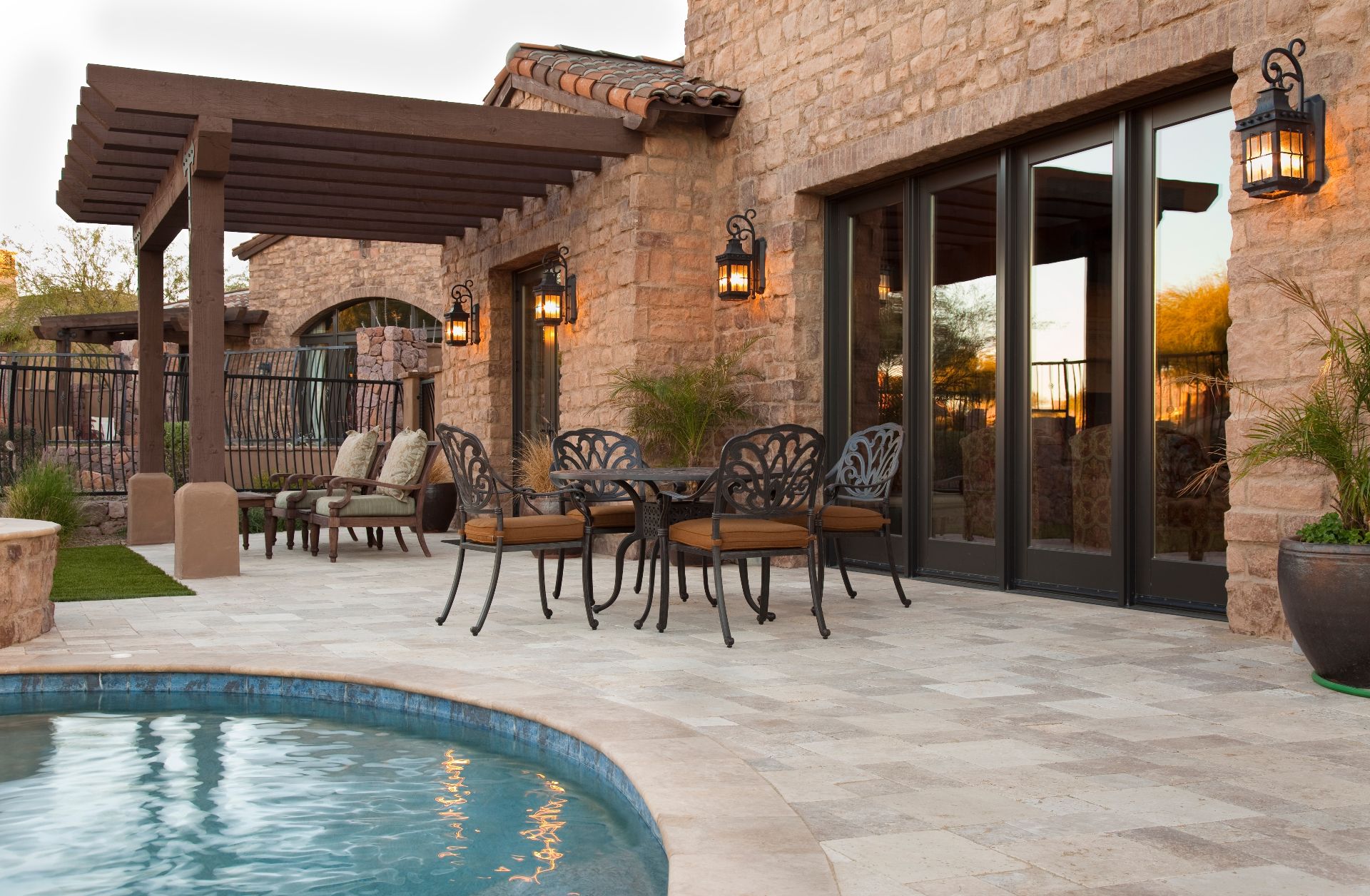 luxury outdoor patio, glass sliding doors, wrought iron furniture, rustic stone facade, Mediterranean-style backyard, cozy pergola, a stylish outdoor dining area, and a scenic poolside setting