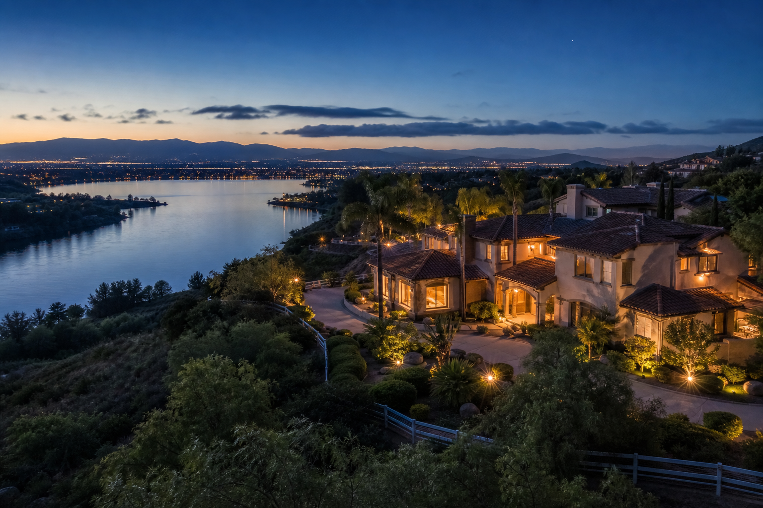 Aerial dusk view of hillside homes overlooking a lake in Southwest Riverside County with valley city lights in the distance