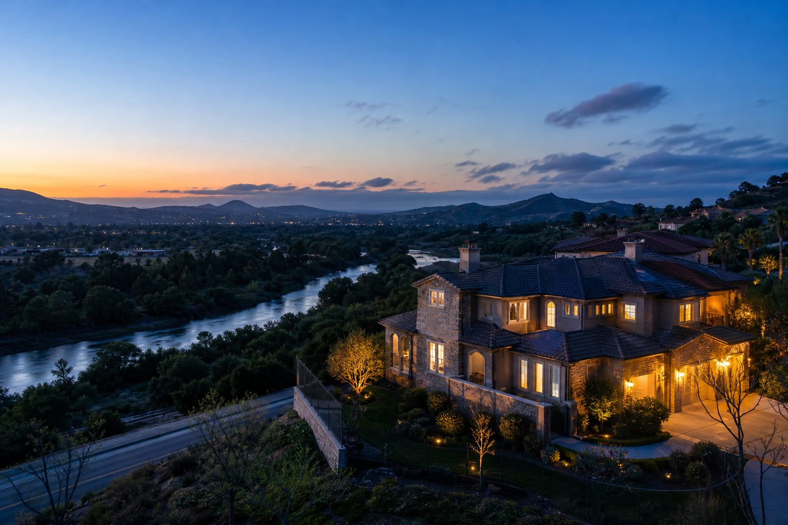 Hillside luxury home lit up at dusk above a Temecula valley with distant mountains