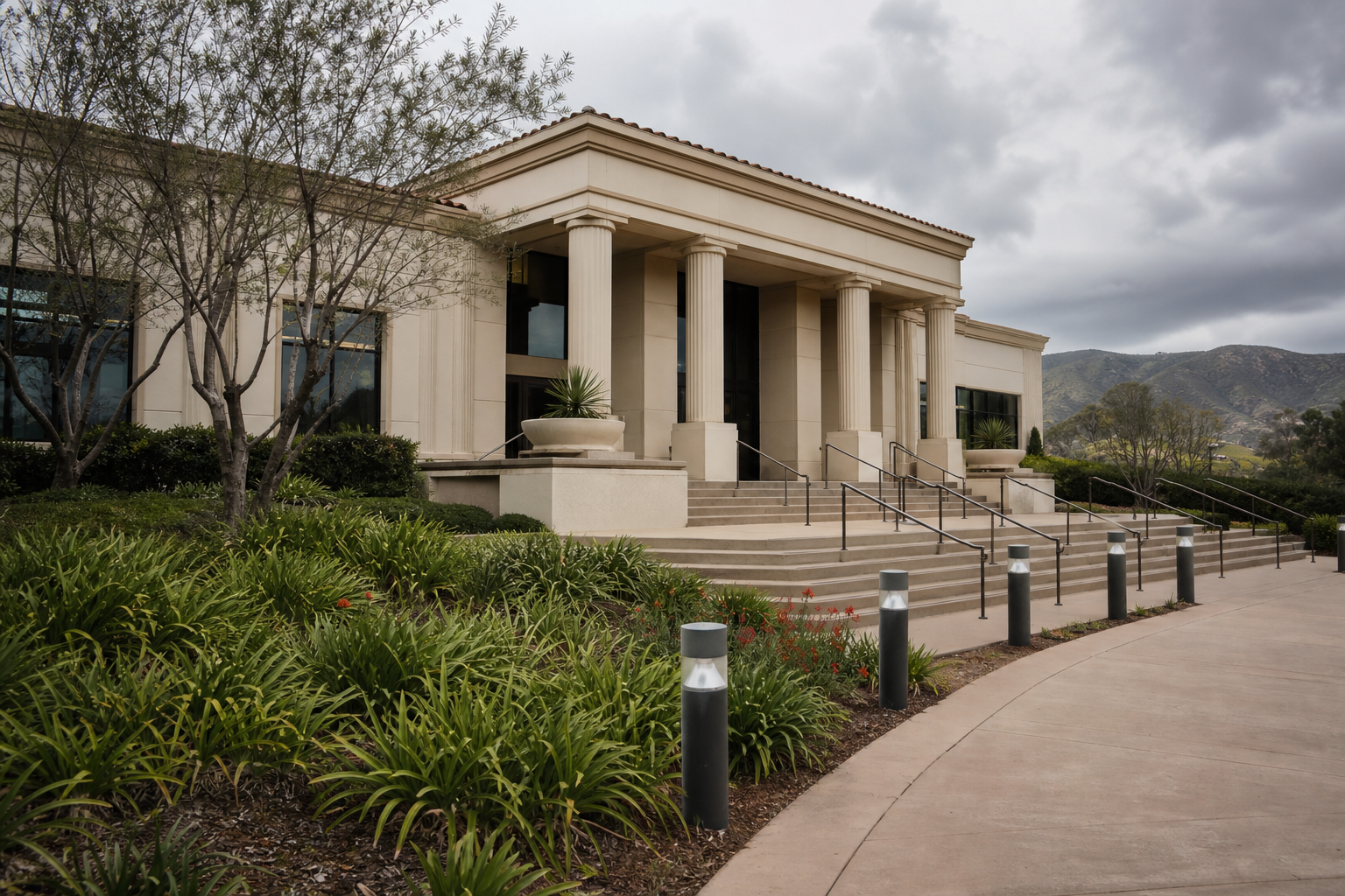 Stone civic building with a columned entrance and curved walkway lined with bollards under a cloudy sky in South Temecula
