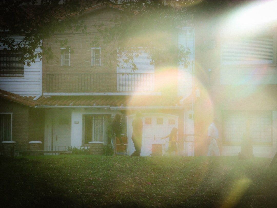 Homeowner stands on their lawn with a contemplative expression, looking at the front of their suburban home, considering t...