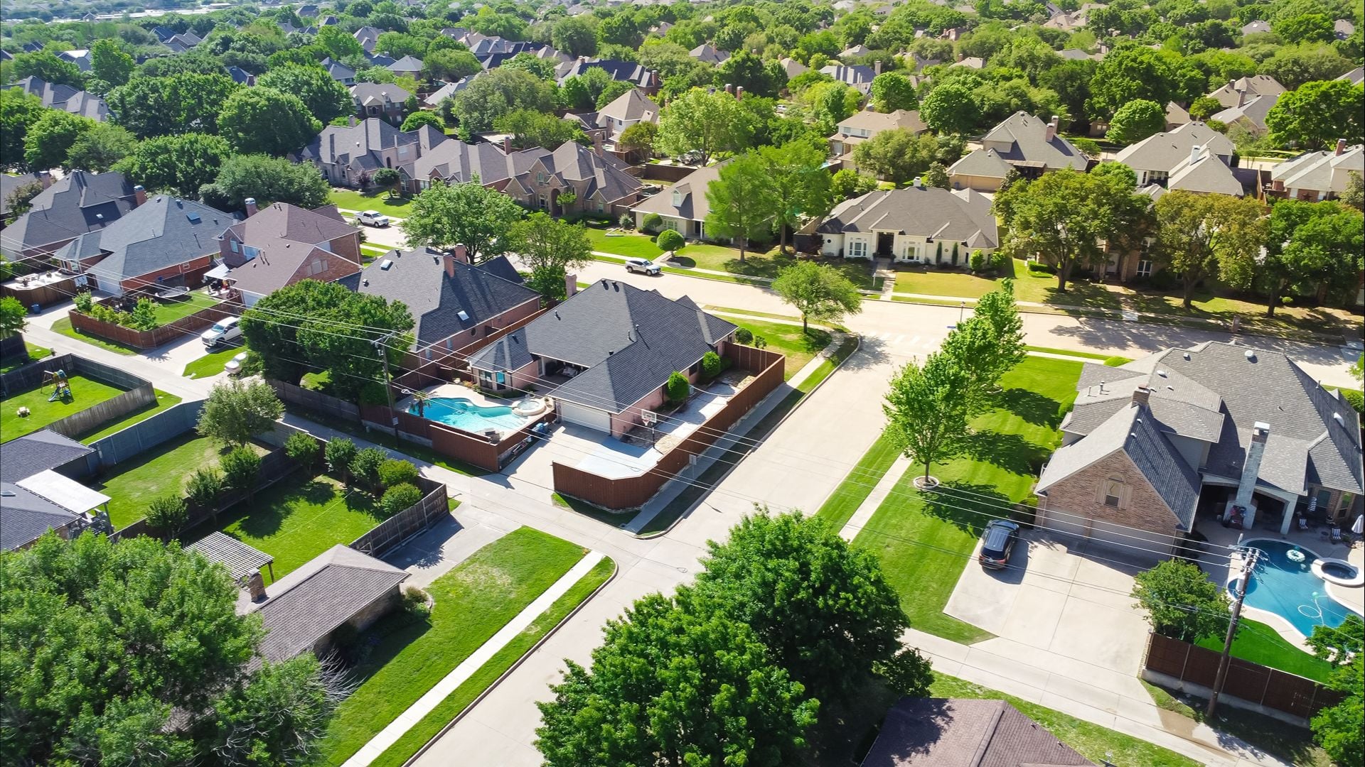 Two story suburban single-family home with swimming pool, large backyard, tall wooden fence in suburb Dallas, Texas subdivision, upscale house lush greenery tree, well-trimmed landscape, aerial. USA