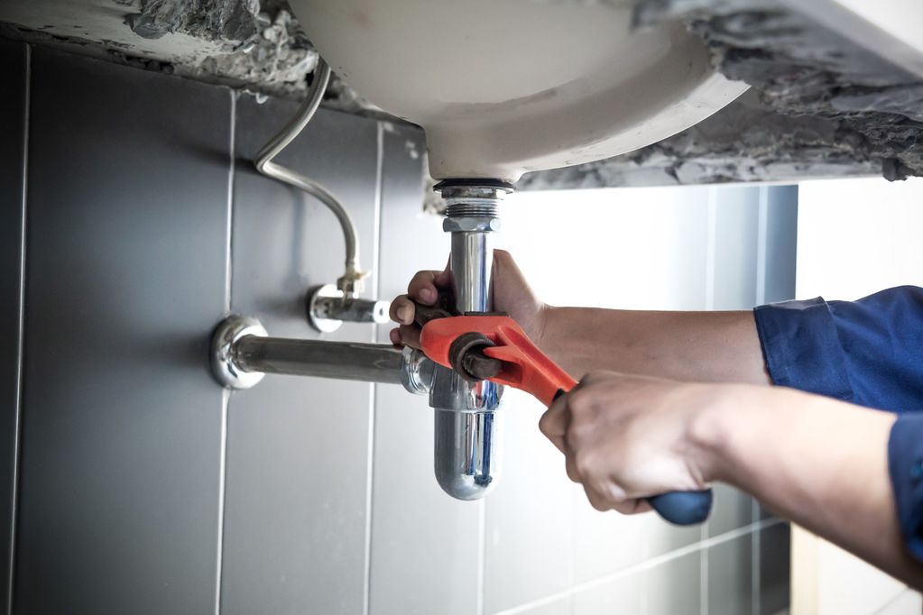 Plumber uses wrench to repair water pipe under sink There is maintenance to fix the water leak in the bathroom.with red wrench, plumbing install concept. (1)