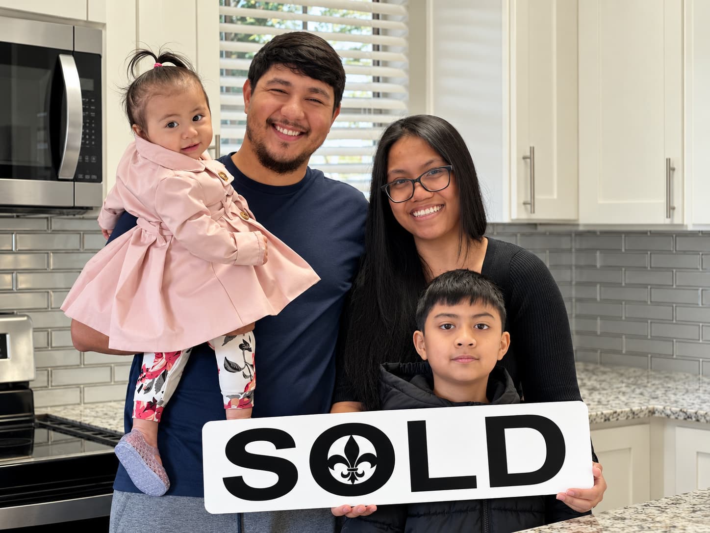 A family holds a sold sign in a modern kitchen.