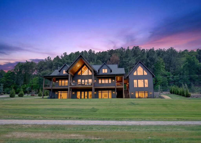 A large, dark-colored house with multiple levels and large windows at dusk.