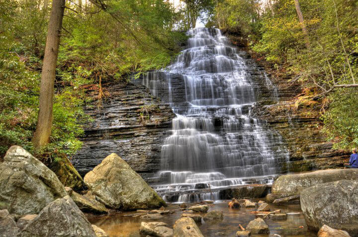 A wide, tiered waterfall cascades down a rocky, forested hillside.