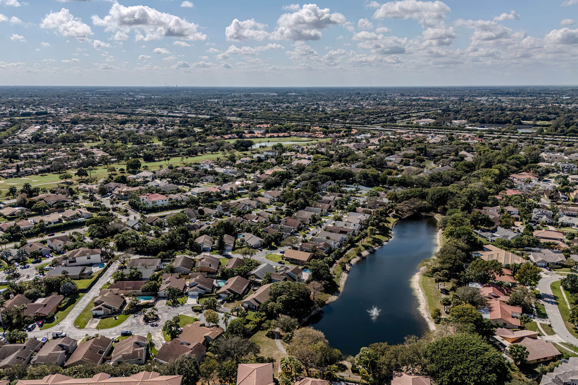 Aerial view of a suburban neighborhood with homes surrounding a dark blue lake with a fountain.