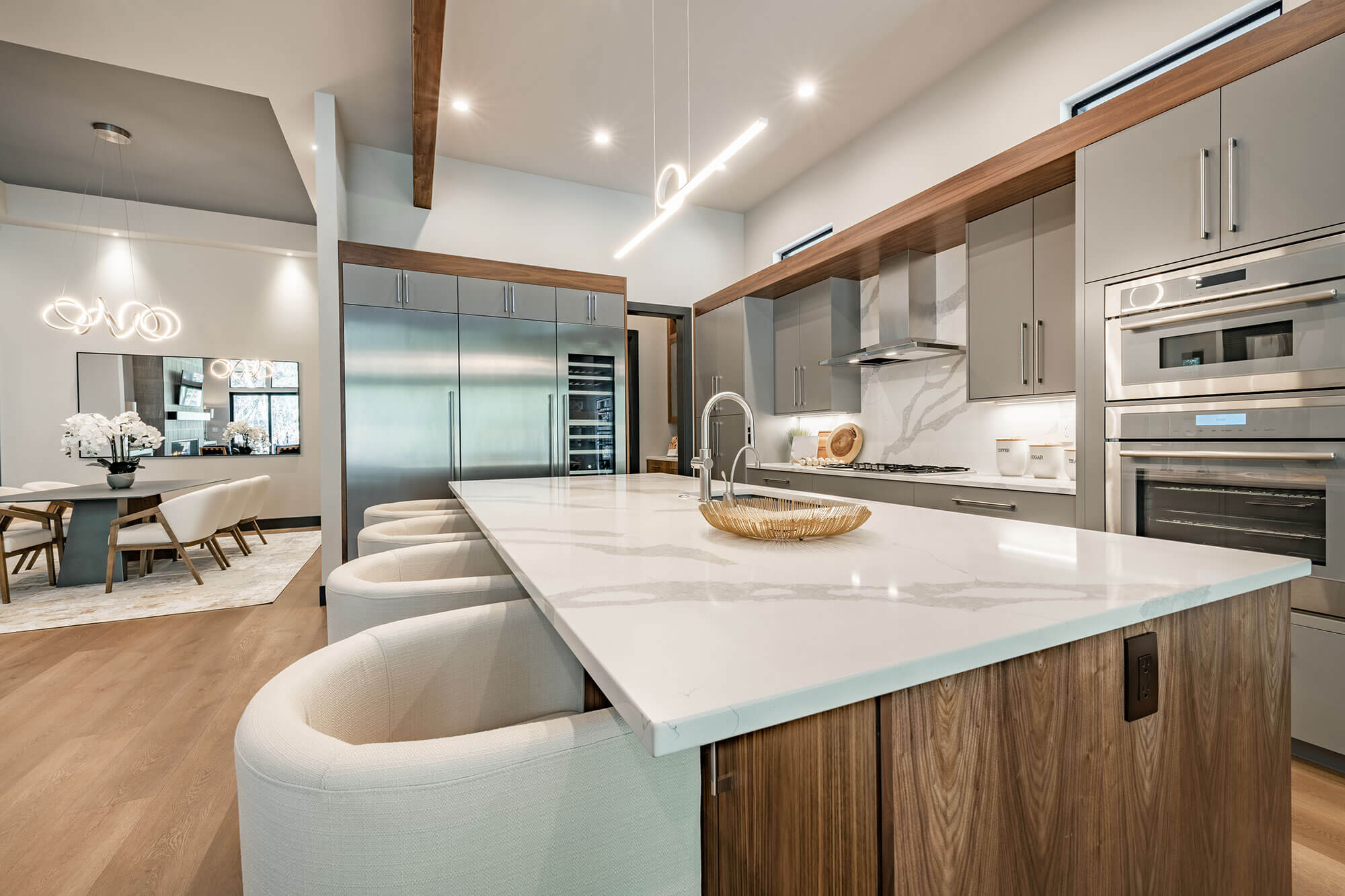 A modern kitchen island with white counter stools and a dining area in the background.