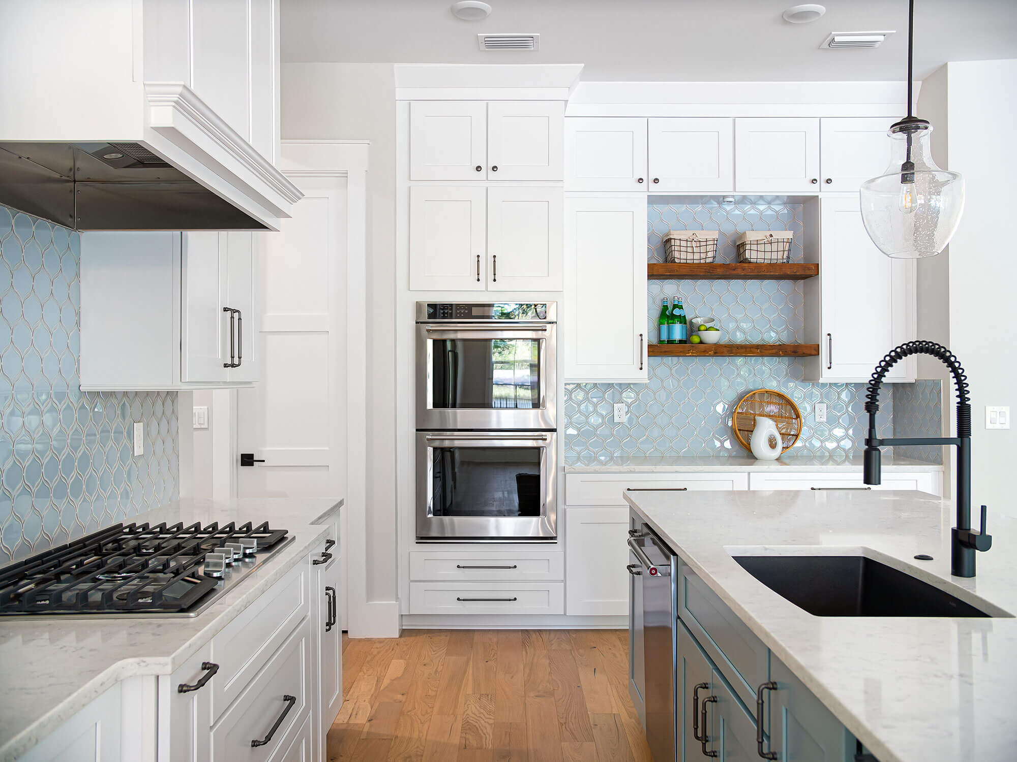 A modern kitchen with white cabinets, a gas stove, and a blue scale tile backsplash.