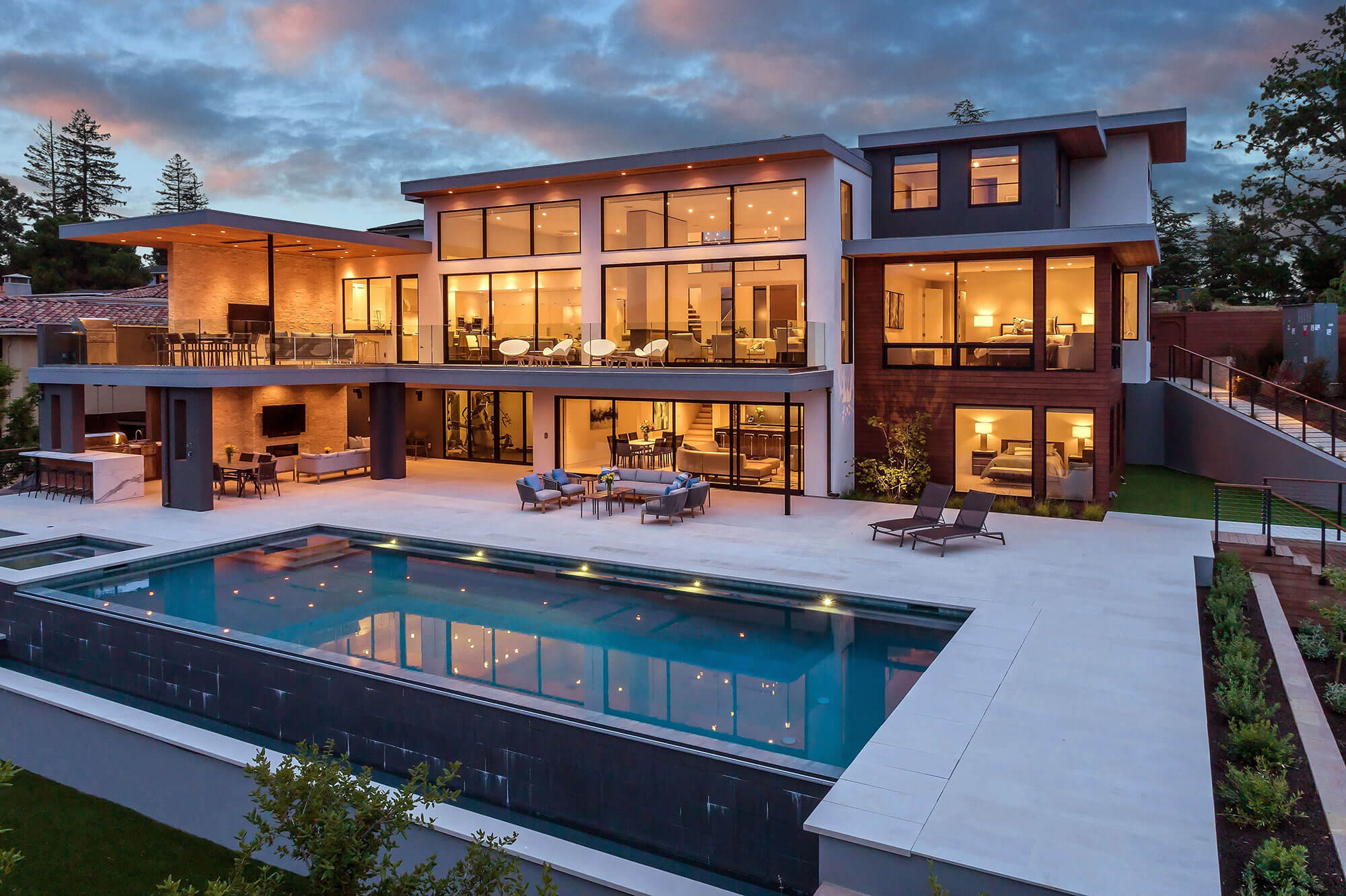 Modern luxury home with expansive windows, multiple balconies, and a large swimming pool.