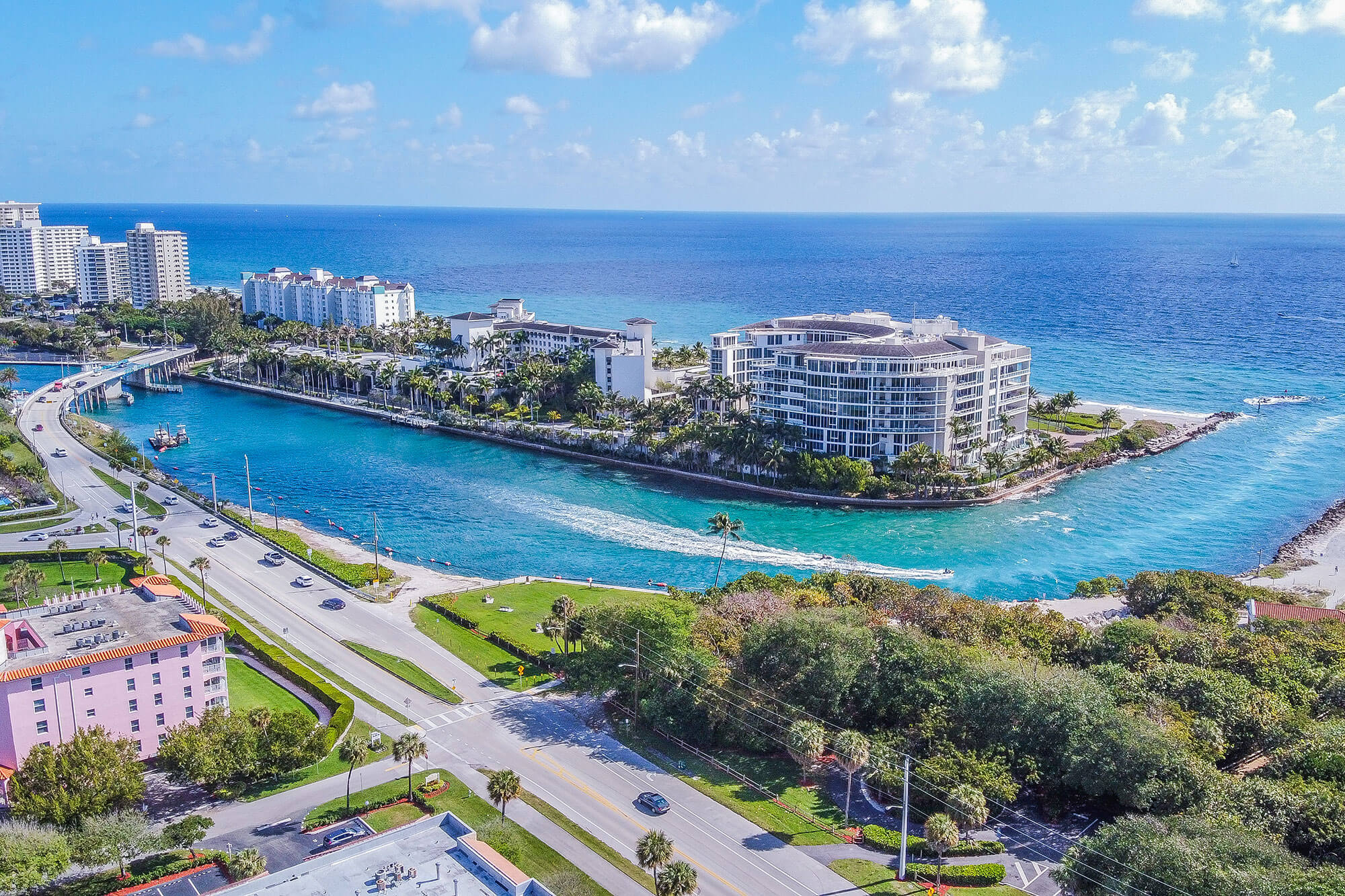 Aerial view of modern waterfront buildings along a blue waterway with boats and a bridge.