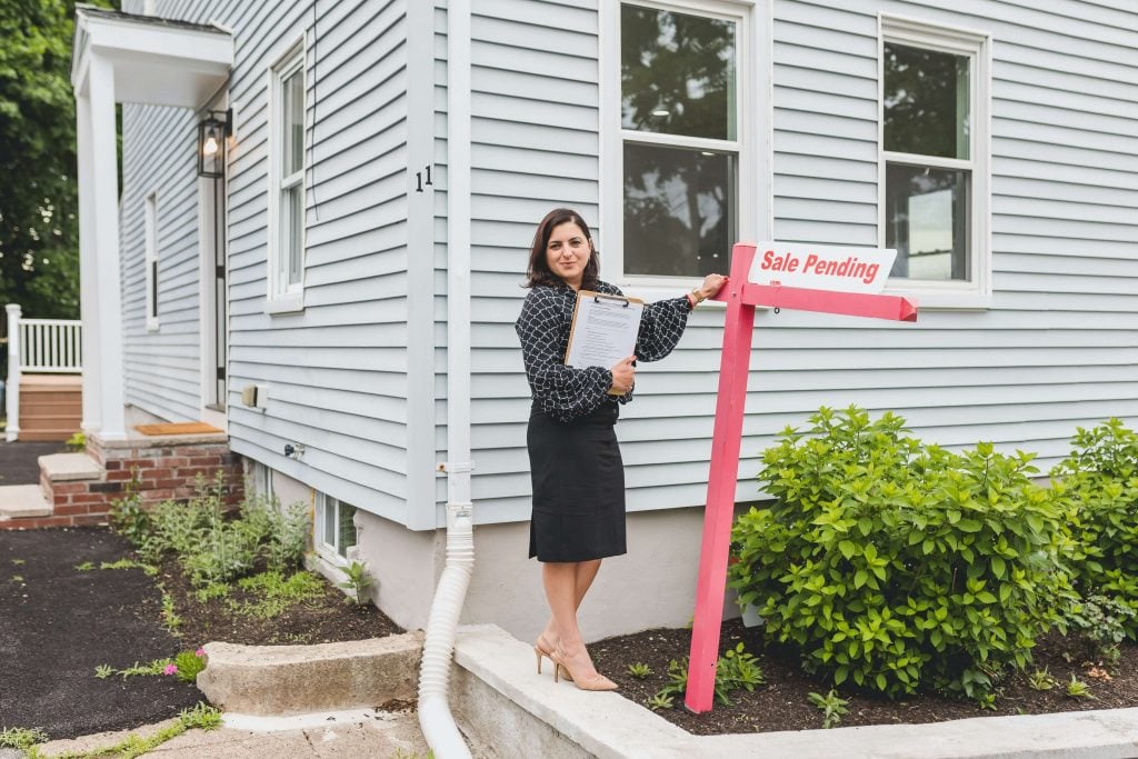 real estate broker stands next to sale pending sign