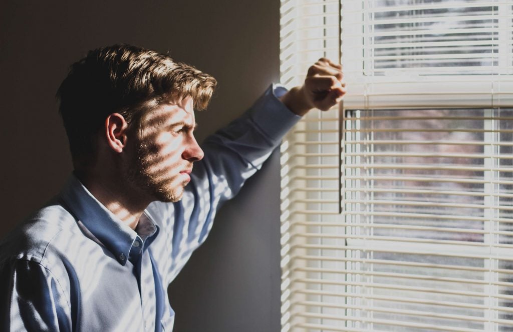 Man stands pensively by window in shadows