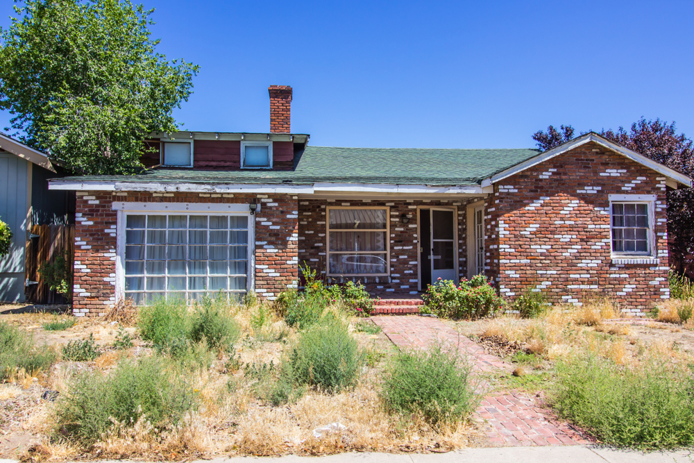 Vacant brick home with overgrown front yard after foreclosure