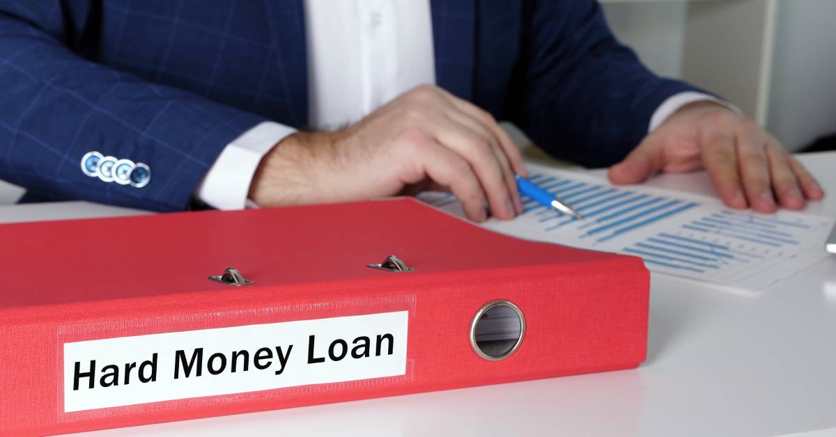 A businessman looking over financial documents next to a binder labeled "HARD MONEY LOAN" on the spine.