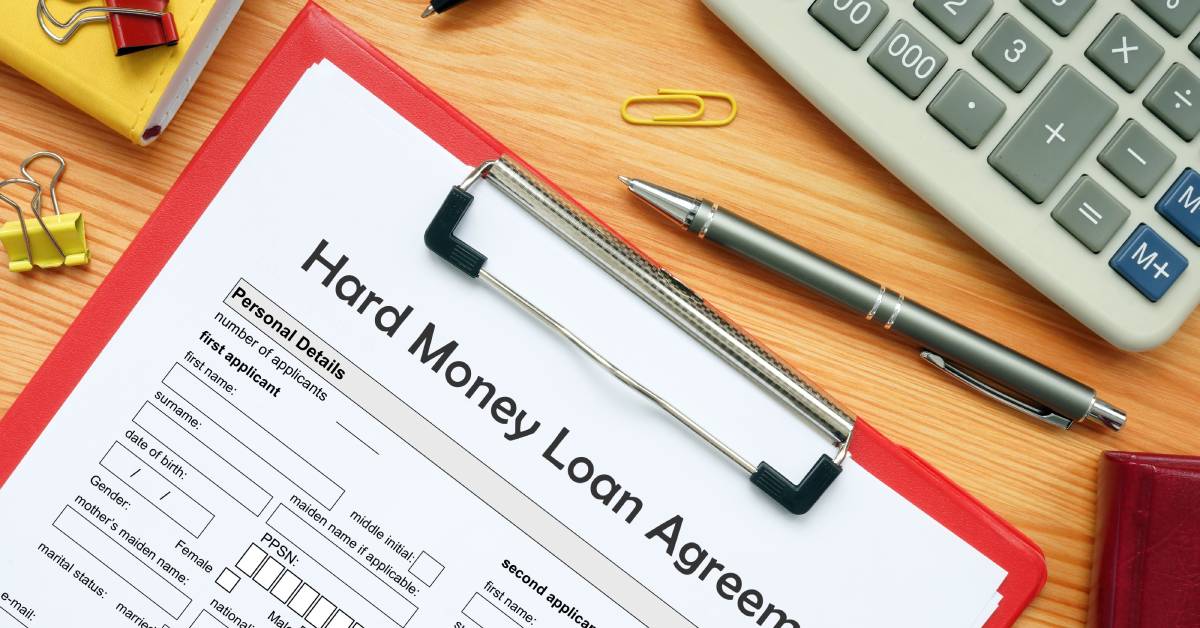 A paper copy of a printed hard money loan agreement attached to a red clipboard and resting on a cluttered desk.