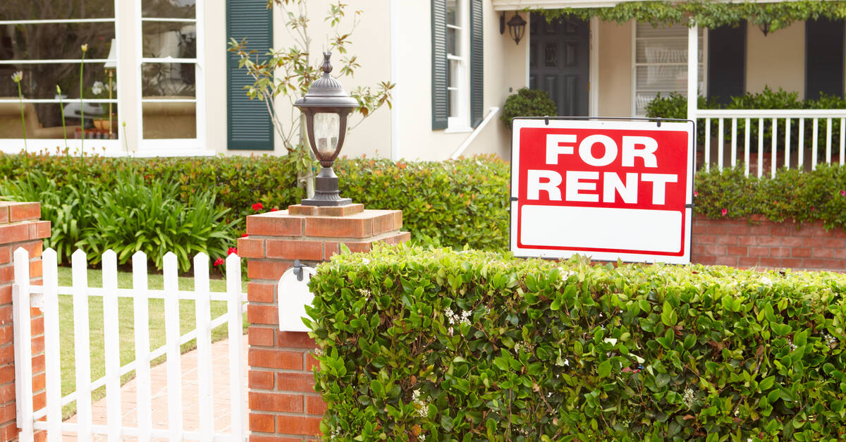 The front of a single-story home from the outside, showcasing a "FOR RENT" sign stuck into the front lawn.