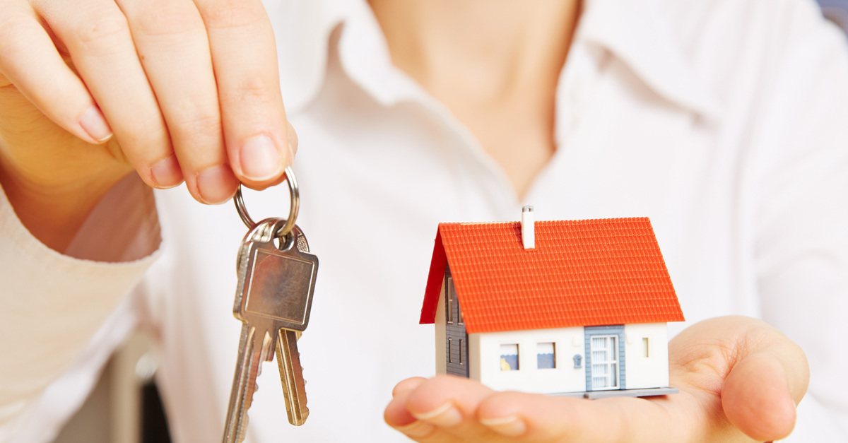 A woman in a white dress shirt holding up keys on a ring in one hand and a small model of a home in her other hand.