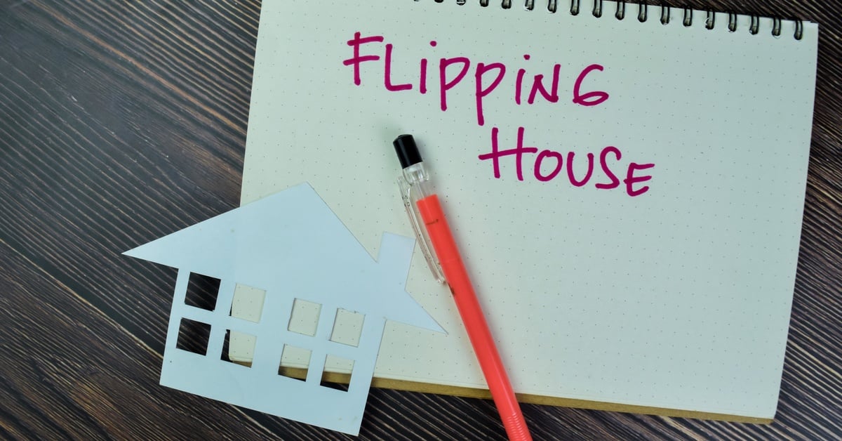 A paper cutout of a house and a pen resting on an open notebook that reads “Flipping House” in red ink.