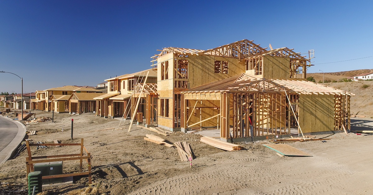 A row of homes that are framed and surrounded by dirt. Next to these homes are a few fully finished houses.